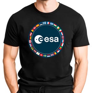 May include: A black t-shirt featuring a circular graphic on the chest. The center of the circle is dark blue with the white text "esa" and a stylized white crescent moon logo. A ring of various international flags surrounds the central logo.