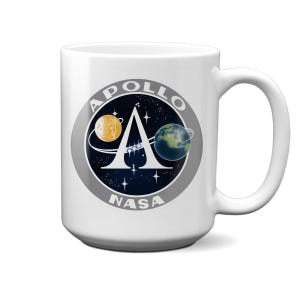 May include: White ceramic mug with a black and white NASA Apollo mission logo featuring a stylized letter A, a crescent moon, and a planet Earth. The logo is surrounded by a gray circle with the words "APOLLO" and "NASA" in white.