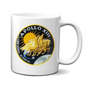 May include: White ceramic mug with a black and yellow Apollo XII mission patch. The patch features three horses running with a sun and moon in the background. The text "Apollo XII" is in a black circle with the text "Ex Luna, Scientia" in a black arc around the circle.