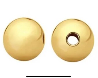 May include: Two gold-colored round beads with a hole in the center. The beads are smooth and shiny.