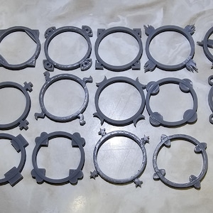 May include: A collection of gray, circular, decorative frames with various designs. The frames are made of a solid material and feature different shapes and patterns around the circular openings. The designs include geometric shapes and stylized elements.