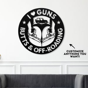 May include: Black and white metal wall art with a circular design. The circle features a heart with the word "GUNS" inside, a silhouette of a jeep, and the words "BUTTS & OFF-ROADIN".