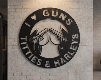 May include: A circular black metal wall sign featuring a cutout design of two handguns pointed toward the center. The text I LOVE GUNS TITTIES & HARLEYS is cut out around the perimeter of the circle, with a heart symbol replacing the word LOVE.