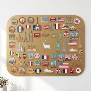 May include: A rectangular gold-toned magnetic display board featuring a collection of travel-themed souvenir magnets. The magnets depict various international landmarks, national flags, city names like Paris, London, Rome, Tokyo, and New York, and a white deer silhouette in the centre.