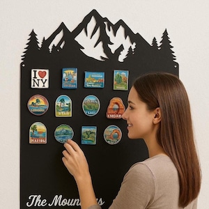 May include: A black metal mountain-shaped display board with souvenir magnets. The magnets depict colourful images of various locations, including "I Love NY," and other scenic destinations. A woman is shown interacting with the display.