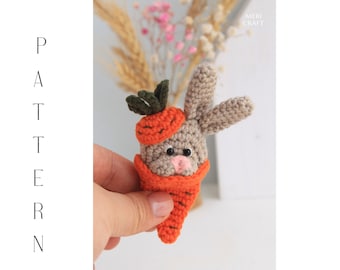 Può includere: Un coniglietto all'uncinetto che indossa un costume da carota. Il coniglietto è grigio e la carota è arancione con foglie verdi.