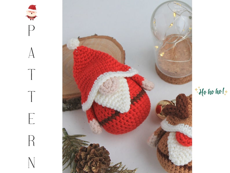 May include: Two crocheted Christmas decorations, one a Santa Claus with a red hat and white beard, and the other a reindeer with brown antlers and a red nose. The decorations are sitting on a wooden surface with a pine cone and a glass jar with lights in the background. The text "Ho ho ho!" is written in green on a white background.