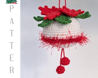May include: White crocheted Christmas ornament with red and green accents. The ornament is shaped like a ball and has a red and white fuzzy trim. It is hanging from a red string with two red pom-poms at the end.