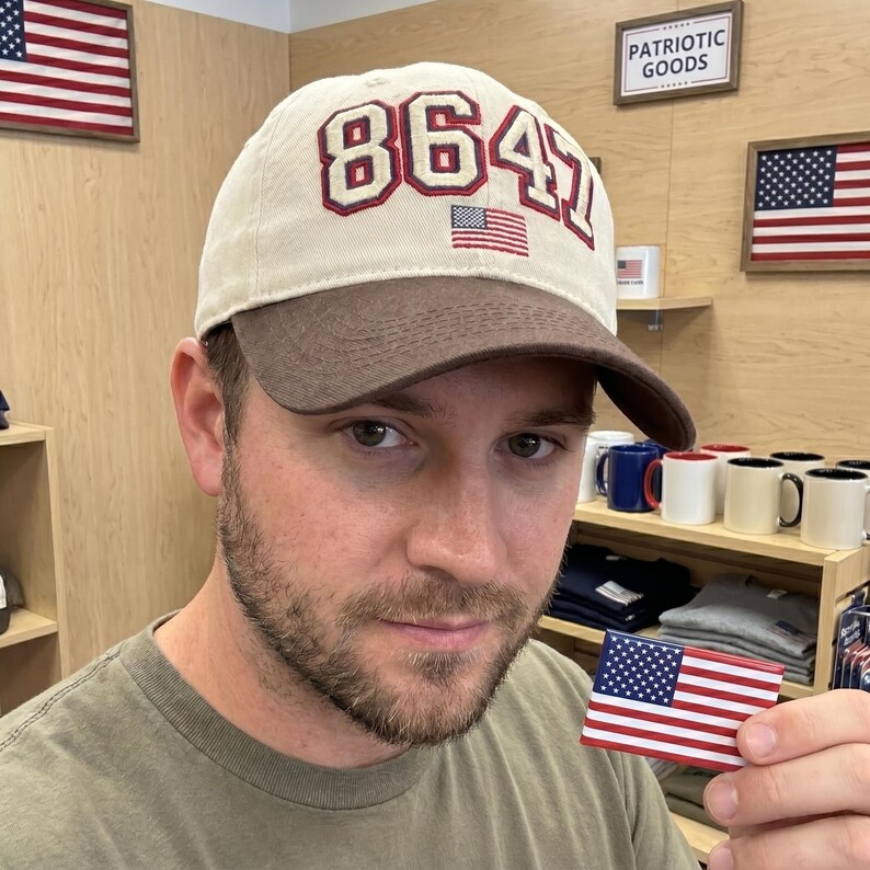 May include: A beige and brown baseball cap with the number "8641" in red and white, and a small American flag. The cap is part of a patriotic goods collection.