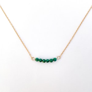 Puede incluir: Un collar de cadena dorada con una fila de cuentas de malaquita verde.
