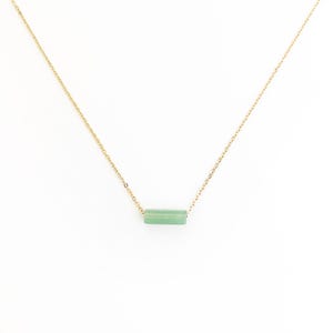 Puede incluir: Un delicado collar de cadena dorada con un colgante de barra de piedra preciosa verde claro.