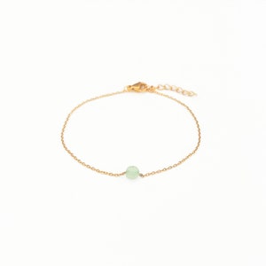 May include: A delicate gold chain bracelet with a single light green gemstone bead.