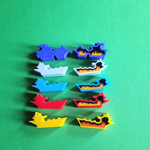 Op de afbeelding: Acht plastic spelstukken in verschillende kleuren, waaronder blauw, wit, lichtblauw, rood, geel en zwart. Elk stuk heeft een ander ontwerp, sommige met vlammen en andere met een eenvoudige vorm.