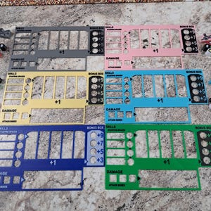 May include: Six different colored character sheets for a tabletop role-playing game. The sheets are made of acrylic and have a variety of compartments for tracking character stats, skills, and damage. The sheets are labeled with the words "Skills", "Starting Spaces", "Bonus Box", and "Damage".