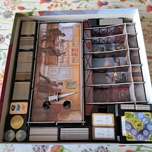 May include: Open board game box with various components. The game board features illustrations of rooms and a bridge. Includes cards, tokens, and other game pieces. The box is set on a floral patterned surface.