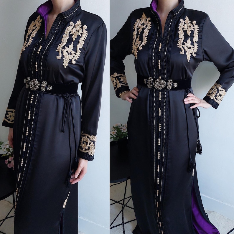 Puede incluir: Un vestido de sat&eacute;n negro con bordados dorados y un cintur&oacute;n de terciopelo negro. El vestido tiene una falda larga y fluida y un escote alto.