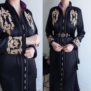 Puede incluir: Un vestido de sat&eacute;n negro con bordados dorados y un ribete morado. El vestido tiene manga larga y un cintur&oacute;n con una hebilla dorada.