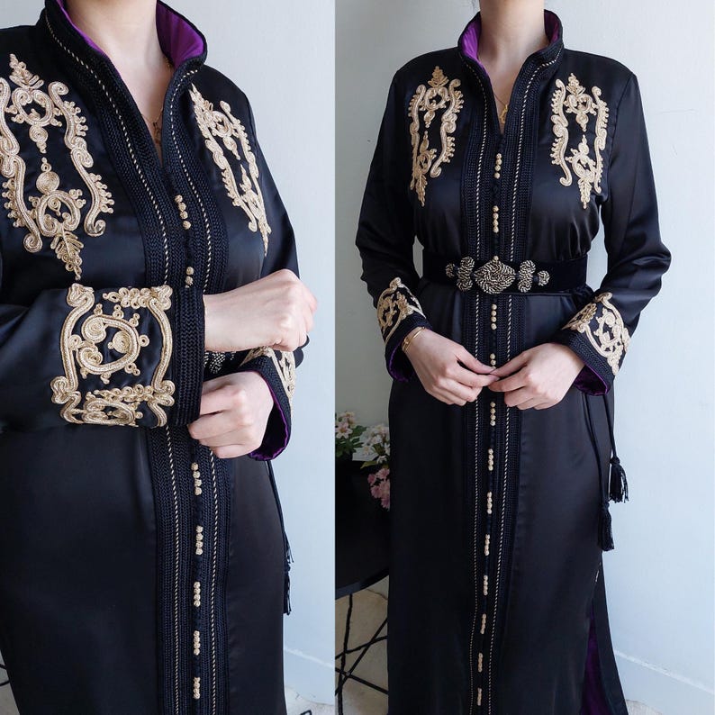 Puede incluir: Un vestido de sat&eacute;n negro con bordados dorados y un ribete morado. El vestido tiene manga larga y un cintur&oacute;n con una hebilla dorada.