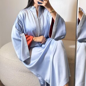 May include: A light blue satin robe with wide sleeves and a mandarin collar. The robe has silver trim along the front and sleeve edges. The inside of the sleeves are a burnt orange color.