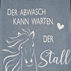 May include: A blue kitchen towel with white text that reads "Der Abwasch kann warten. Der Stall nicht."  A white horse head silhouette is in the center of the towel.