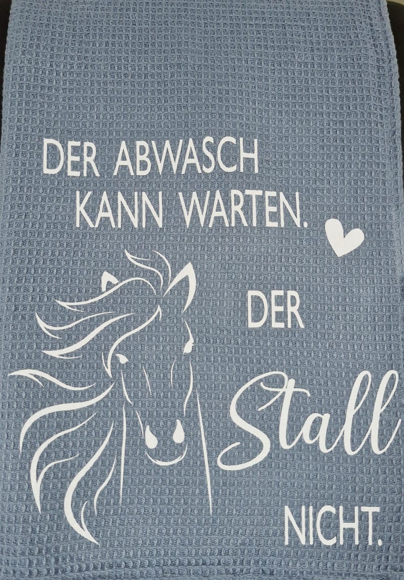 May include: A blue kitchen towel with white text that reads "Der Abwasch kann warten. Der Stall nicht."  A white horse head silhouette is in the center of the towel.