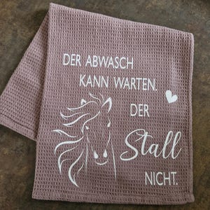 May include: A pink waffle weave kitchen towel with a white horse silhouette and the text "Der Abwasch kann warten. Der Stall nicht."