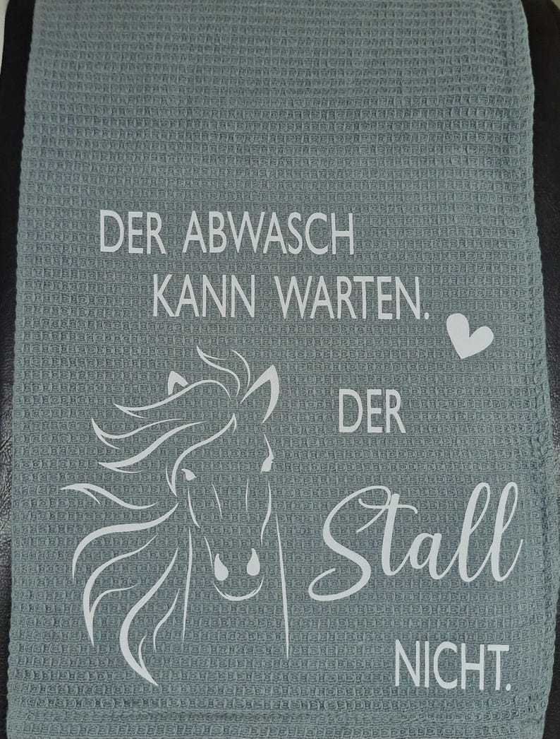 May include: A gray kitchen towel with a white horse design and the text "Der Abwasch kann warten. Der Stall nicht."