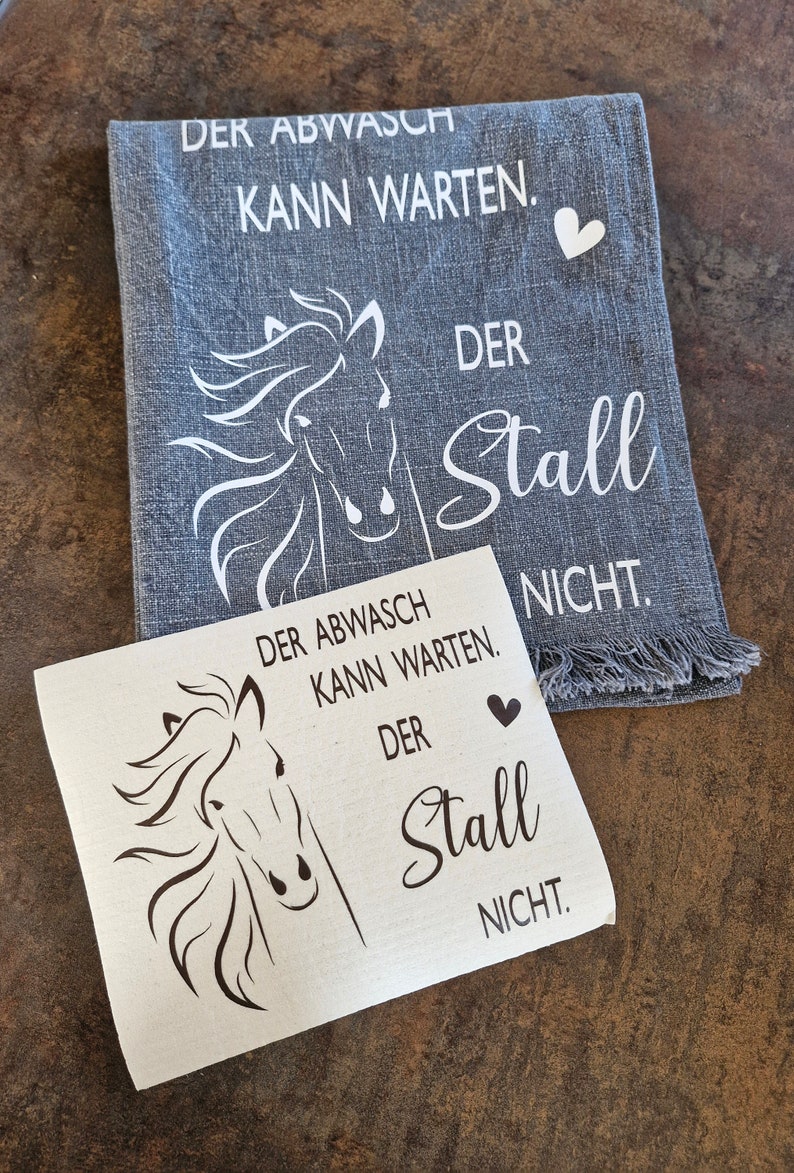 May include: A white horse head design on a gray tea towel with the text "Der Abwasch kann warten. Der Stall nicht."  A second image shows a brown horse head design on a white background with the text "Der Abwasch kann warten. Der Stall nicht."
