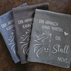 May include: Three gray kitchen towels with white text and a horse design. The text reads "Der Abwasch Kann Warten. Der Stall Nicht."