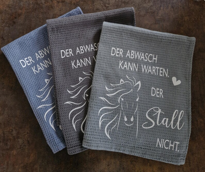 May include: Three gray kitchen towels with white text and a horse design. The text reads "Der Abwasch Kann Warten. Der Stall Nicht."
