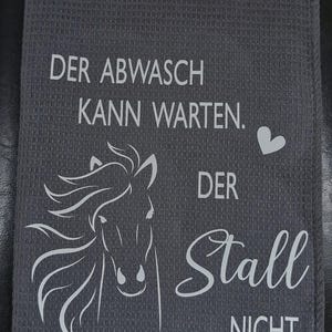 May include: A gray kitchen towel with white text that reads "Der Abwasch kann warten. Der Stall nicht."  A white silhouette of a horse's head is in the center of the towel.