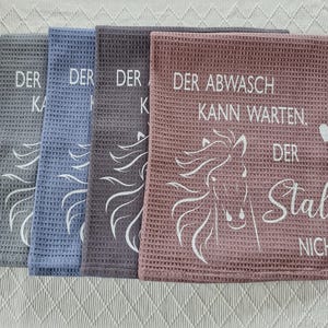 May include: Three kitchen towels with a horse design and the text "Der Abwasch kann warten. Der Stall nicht."  The towels are gray, blue, and pink.