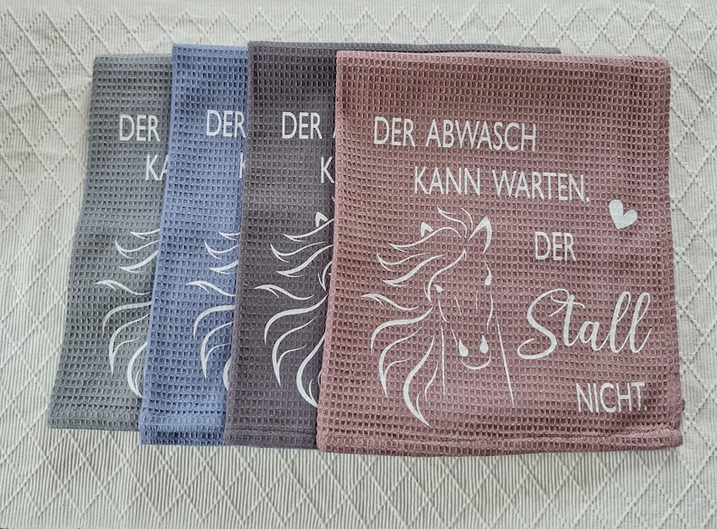 May include: Three kitchen towels with a horse design and the text "Der Abwasch kann warten. Der Stall nicht."  The towels are gray, blue, and pink.
