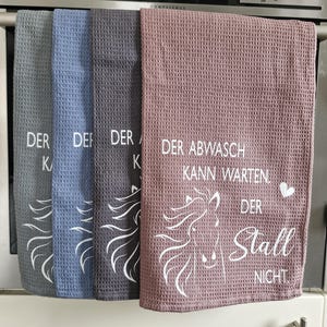 May include: Three kitchen towels with a horse design and the text "Der Abwasch kann warten. Der Stall nicht."  The towels are in blue, gray, and pink.