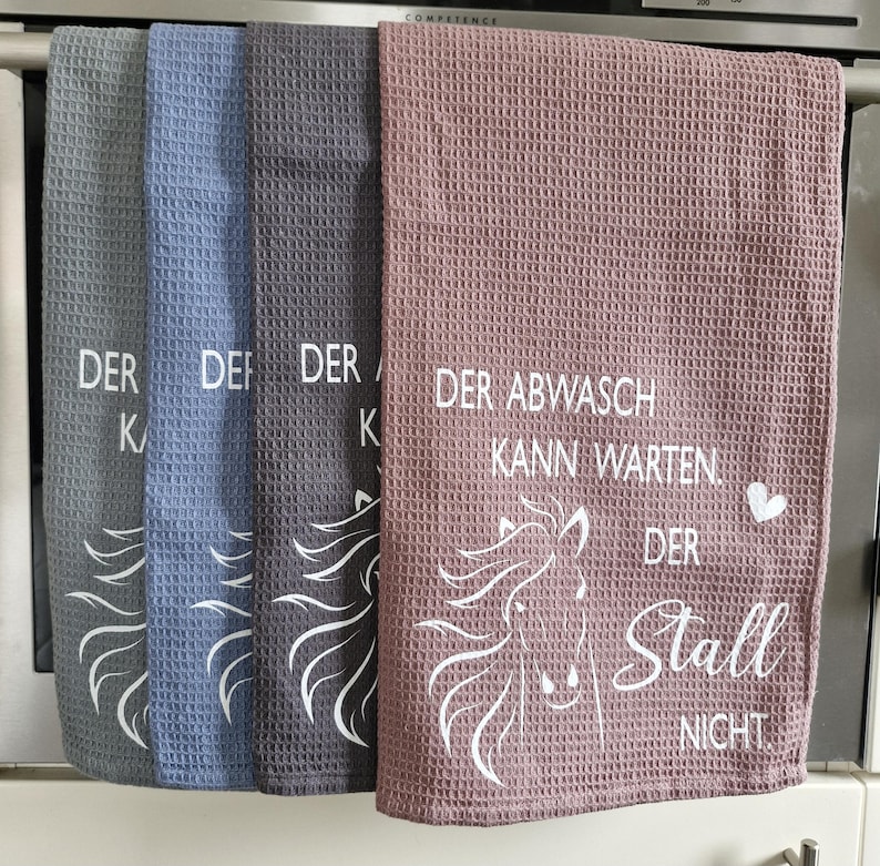 May include: Three kitchen towels with a horse design and the text "Der Abwasch kann warten. Der Stall nicht."  The towels are in blue, gray, and pink.