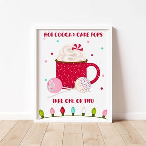 May include: A white printable sign with red text that reads "Hot Cocoa & Cake Pops" and a red mug with white whipped cream and sprinkles. Two cake pops are on sticks with pink and white sprinkles. The sign also has a string of Christmas lights at the bottom.