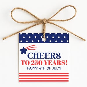 May include: A white gift tag with a blue and red patriotic design, tied with twine. The tag features a blue star with a red comet tail and the text "CHEERS TO 250 YEARS! HAPPY 4TH OF JULY!" in red and blue.