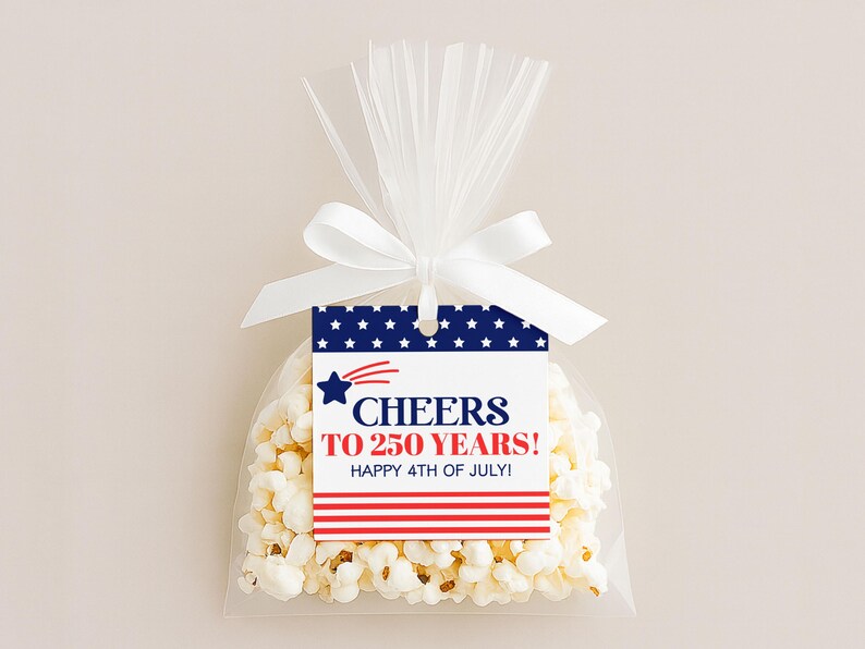 May include: A clear cellophane bag filled with popcorn, tied with a white ribbon. A tag with a blue background and white stars reads "Cheers to 250 Years! Happy 4th of July!" in red and white text, with a red and white striped design.