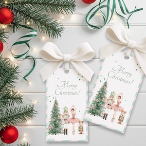 May include: Two gift tags with white bows, featuring a Christmas tree, a ballerina, and a nutcracker. The tags have the text "Merry Christmas!" and are decorated with green and pink stripes. Festive holiday decor.