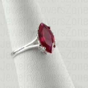 Könnte beinhalten: Ein silberner Ring mit einem großen, markisenförmigen Rubin-Edelstein. Der Ring ist auf einem weißen Hintergrund platziert.