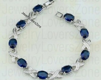 May include: A silver bracelet with a delicate design featuring a series of oval-shaped blue gemstones. The bracelet has a clasp closure and is adorned with small, clear stones.