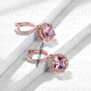 Puede incluir: Un par de pendientes de oro rosa con una piedra preciosa cuadrada rosa rodeada de pequeñas piedras preciosas transparentes. Los pendientes tienen un diseño de aro.