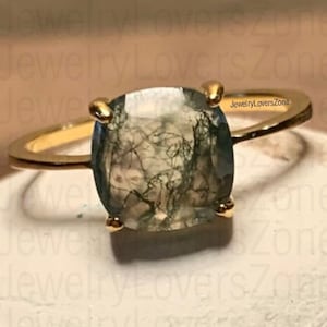 May include: A gold ring with a green and white moss agate gemstone. The ring is set with a cushion-shaped stone.