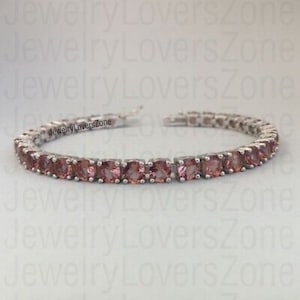May include: A silver bracelet with a row of square-cut, pink gemstones. The bracelet is shown against a white background. The gemstones are set in a silver metal setting.