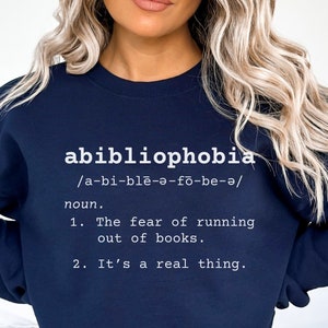 Puede incluir: Una sudadera azul marino con la palabra "abibliophobia" y su definición impresa en blanco. La definición es "El miedo a quedarse sin libros. Es algo real."