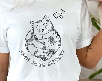 以下が含まれることがあります： 猫が地球を抱きしめている黒い線画が描かれた白いTシャツ。猫の下に「Love Your Mother」という文字が書かれています。