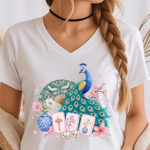 May include: A white V-neck t-shirt featuring a colorful graphic print of a peacock with vibrant blue and green feathers, a folding fan with crane illustrations, a blue and white vase, three mahjong tiles, two dice, and pink floral accents.