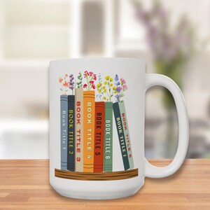 Left hand side of White 15 oz mug with seven books on a shelf with wildflowers for bookmarks. Book titles can be customized to a person's favorite books.