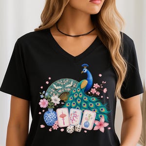 May include: A black V-neck t-shirt featuring a vibrant graphic print of a blue peacock with a fanned tail, a folding fan with cranes, a blue and white porcelain vase, three mahjong tiles, two dice, and pink cherry blossom flowers.