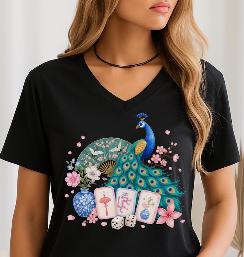 May include: A black V-neck t-shirt featuring a vibrant graphic print of a blue peacock with a fanned tail, a folding fan with cranes, a blue and white porcelain vase, three mahjong tiles, two dice, and pink cherry blossom flowers.
